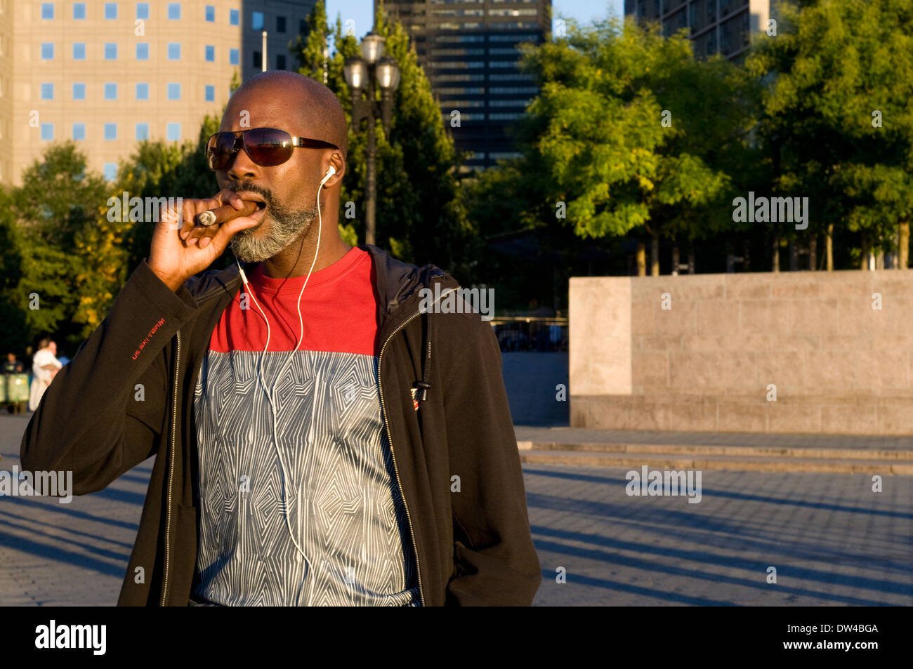Un Américain fume un cigare dans Battery Park. Ce parc est dans le sud-ouest du centre-ville de Manhattan, à proximité du quartier financier et de masse nulle. Dans la région de Battery Park City's de nombreux restaurants, il vaut la peine de prendre un "brunch" à regarder le fleuve et les bâtiments de New Jersey, et une grande promenade le long de l'Hudson. Dans ce parc, nous pouvons voir le château Clinton ou prendre le ferry menant à Liberty Island (où la célèbre Statue de la Liberté et Ellis Island). Banque D'Images