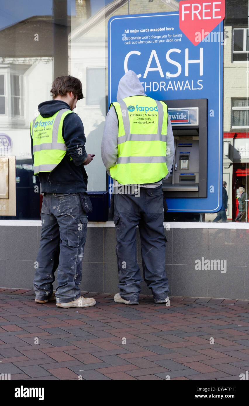 Deux jeunes hommes en vêtements de travail constructeurs retirer de l'argent à un distributeur automatique de Nationwide Building Society ou Cash Machine Banque D'Images