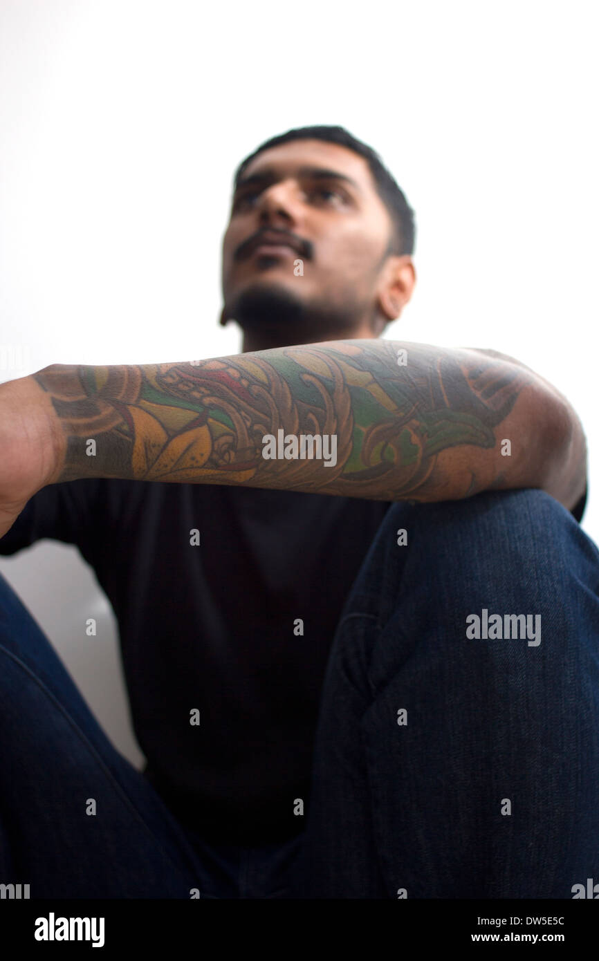 Indien avec tattoo accroupis contre un mur Banque D'Images