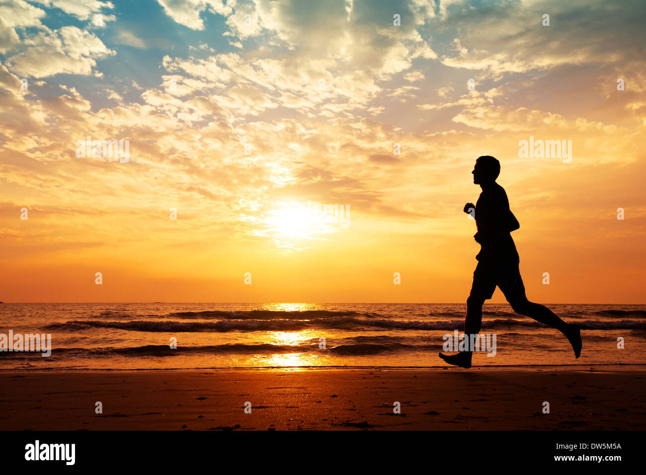 Silhouette d'homme qui court sur la plage au coucher du soleil Banque D'Images