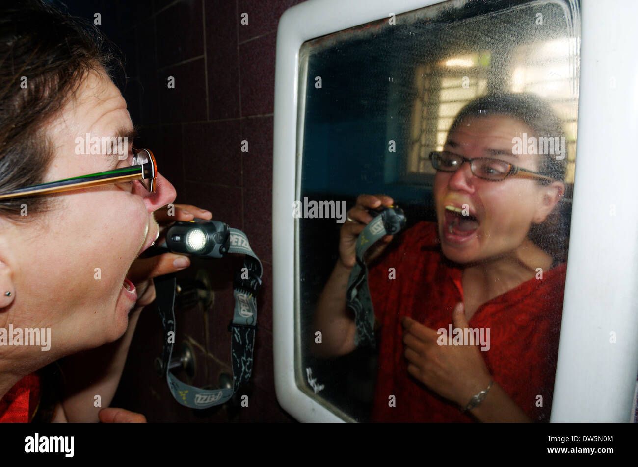 Une femme contrôle de son mal de gorge avec une lampe frontale dans un miroir Banque D'Images