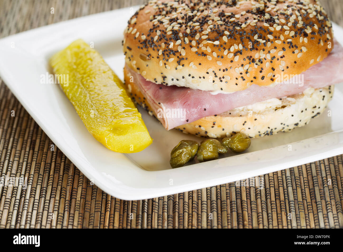 Photo horizontale d'un sandwich au jambon avec des câpres et cornichons tranchés sur plaque blanche avec bambou sous Banque D'Images