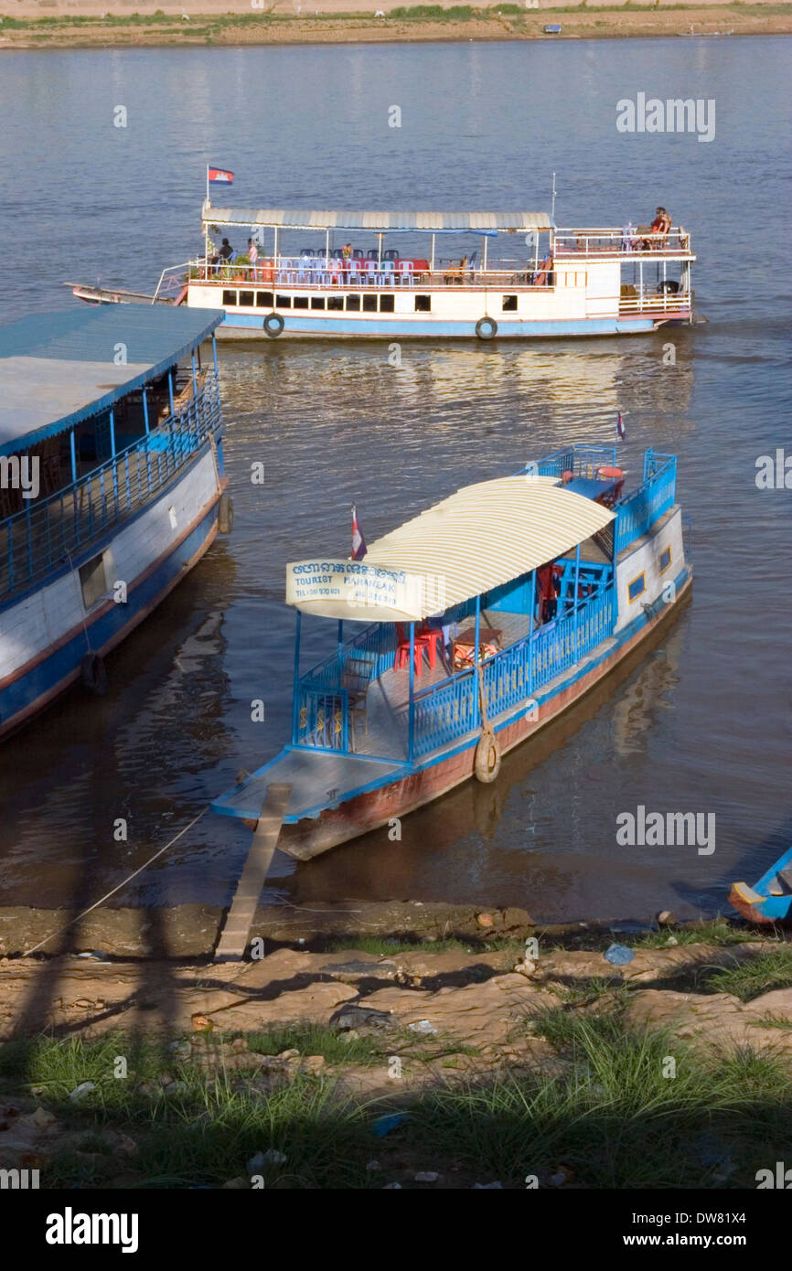Un bateau de croisière touristique passe d'autres bateaux qui sont amarrés à la rive du Mékong à Phnom Penh, Cambodge. Banque D'Images