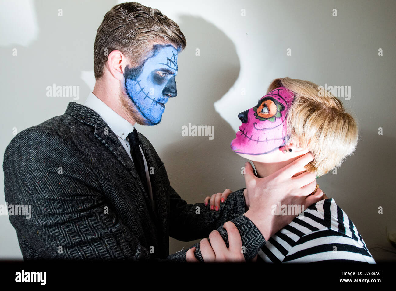 L'homme dans un beau jeune couple avec style horreur face paint fait semblant d'étrangler la femme, photographiée en blanc. Banque D'Images