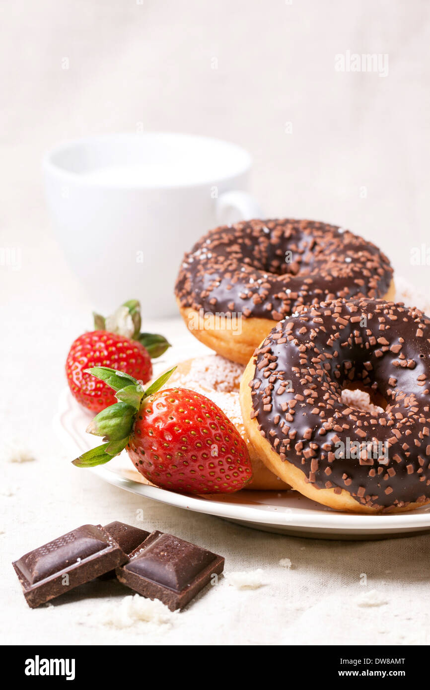 La plaque avec des beignets au chocolat, fraises et chocolat noir servi avec une tasse de lait sur textile blanc Banque D'Images