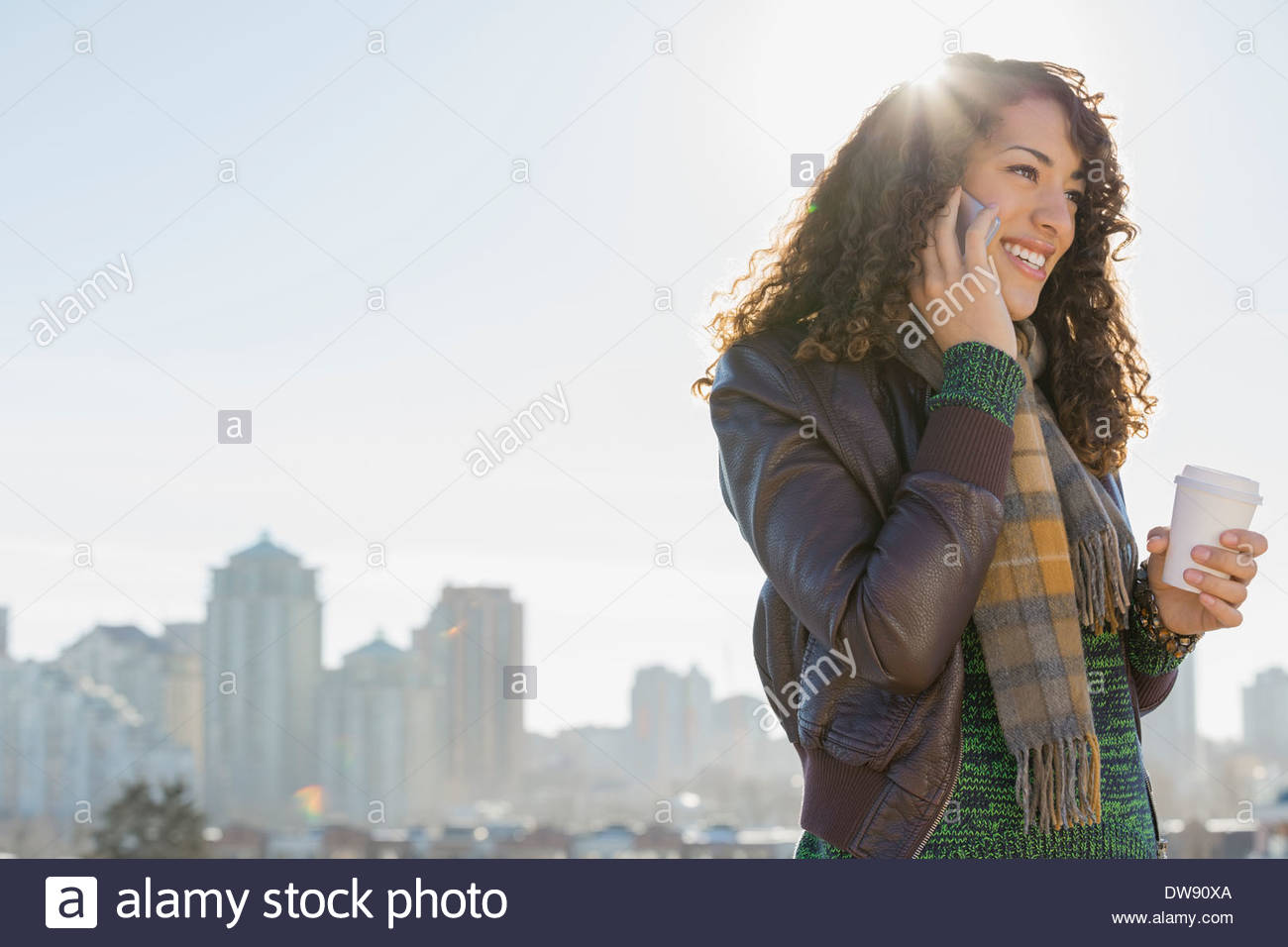 Smiling woman répondre à smart phone contre cityscape Banque D'Images