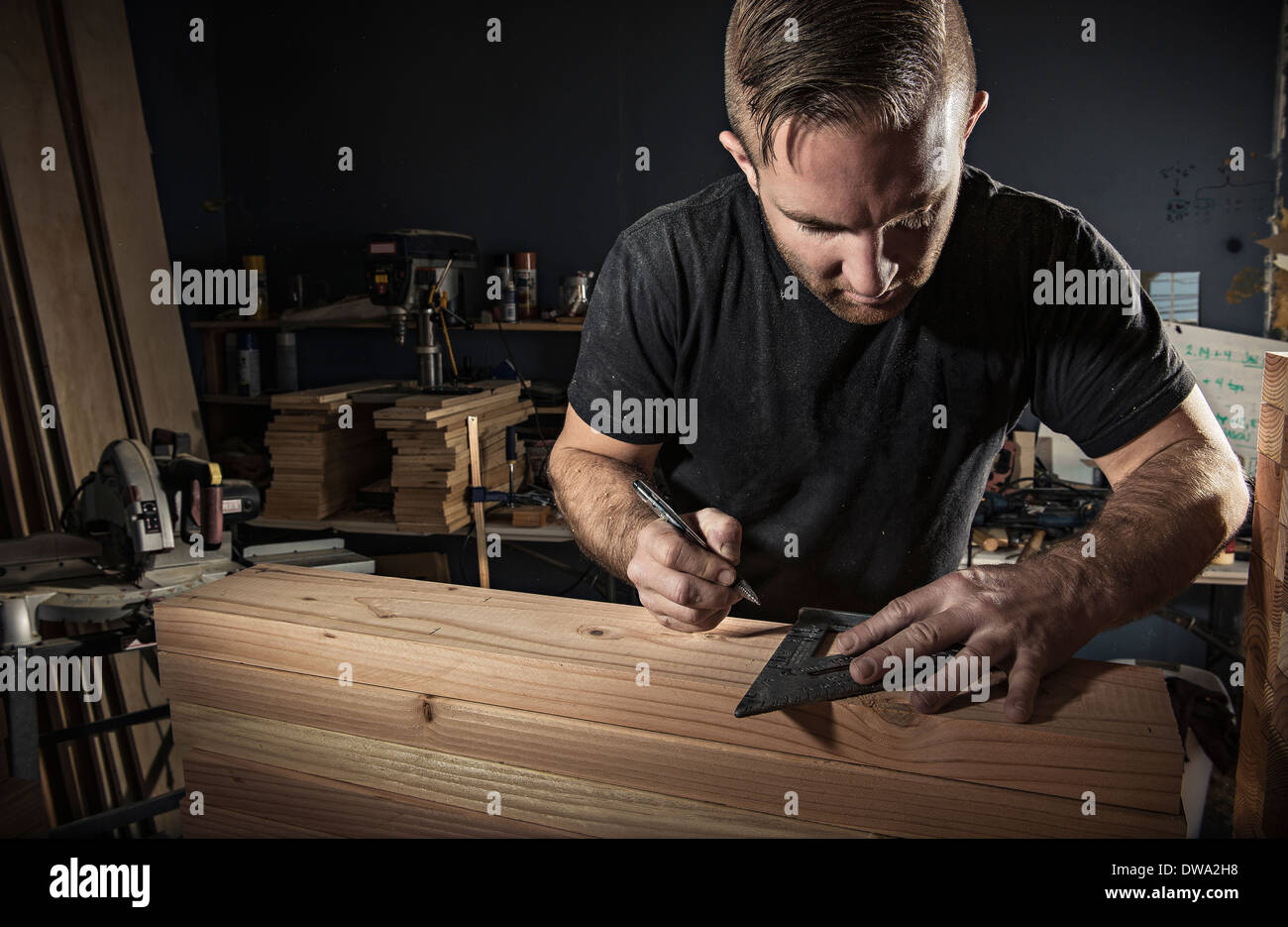 Male carpenter measuring wooden plank avec équerre en atelier Banque D'Images
