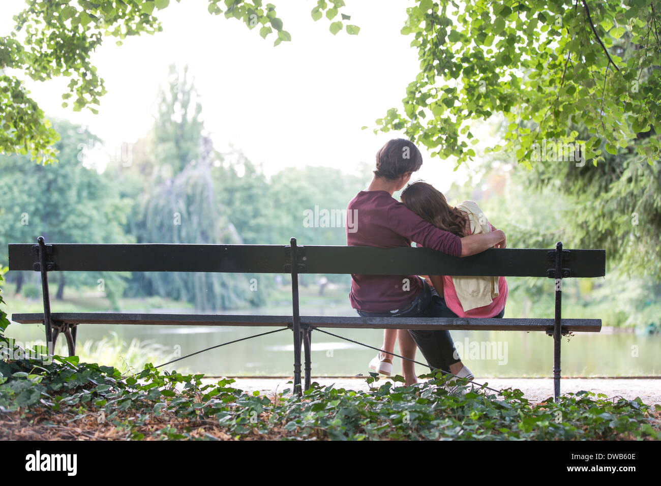 Vue arrière du romantic young couple sitting on bench at lakeside Banque D'Images