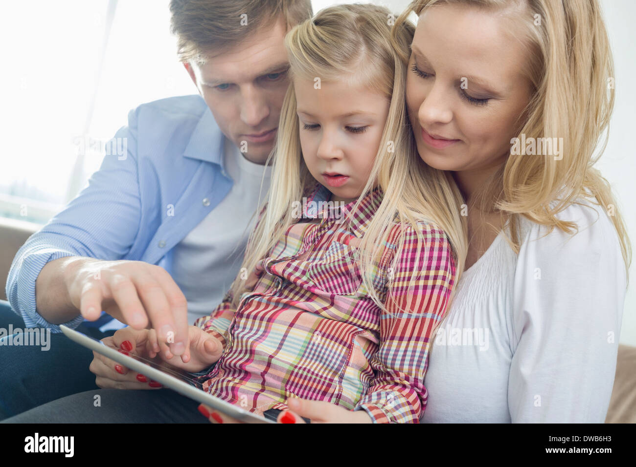 Les parents et la fille using tablet computer in living room Banque D'Images