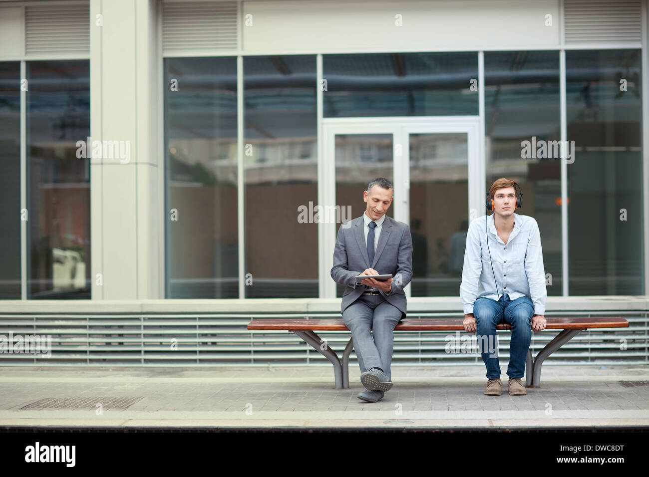 D'affaires et un jeune homme assis sur le banc de la gare Banque D'Images