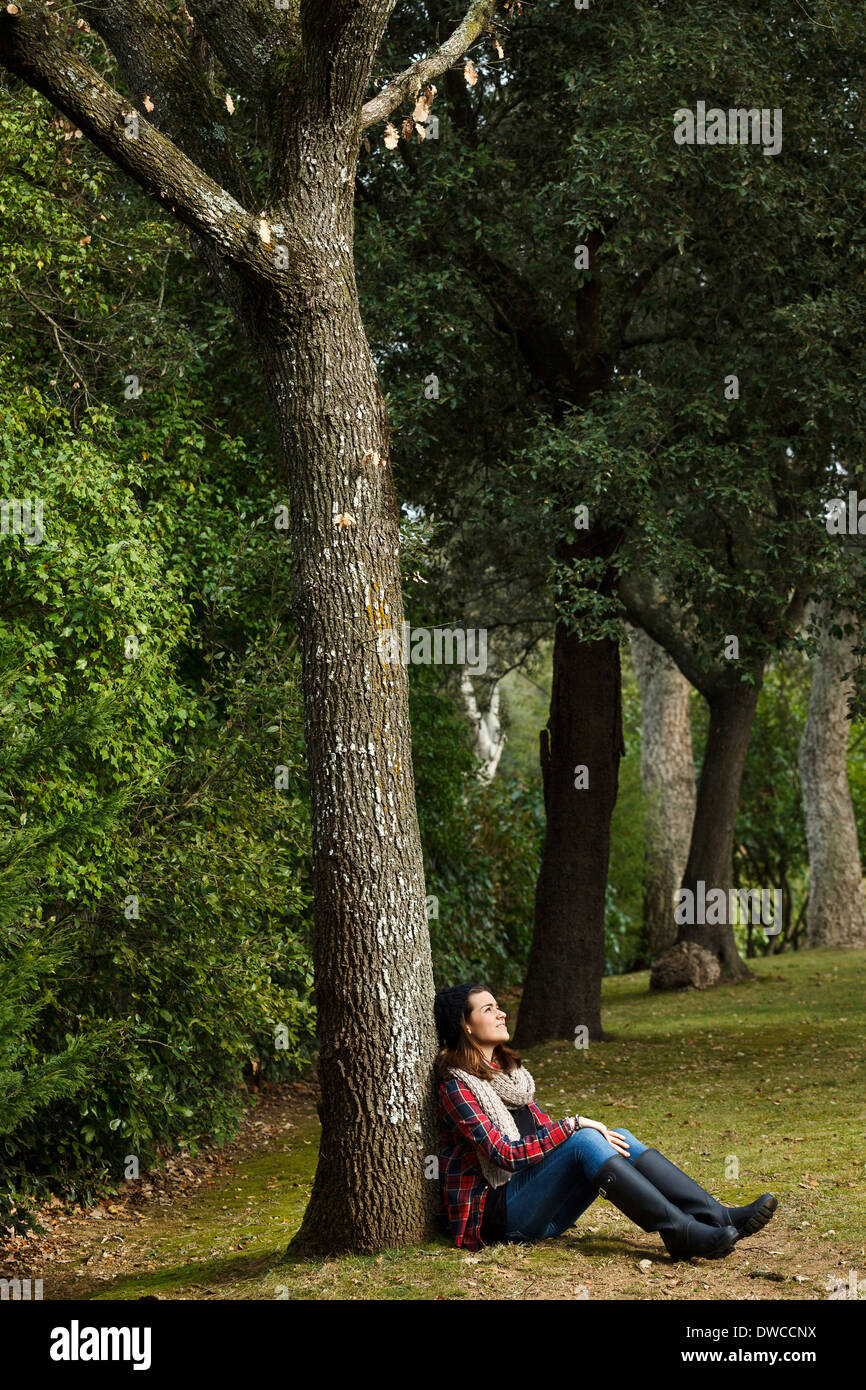 Teenage girl sitting against tree in forest Banque D'Images