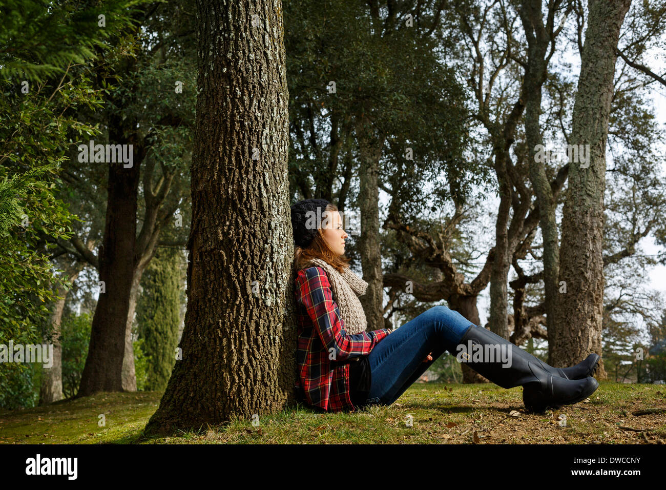 Teenage girl sitting against tree in forest Banque D'Images