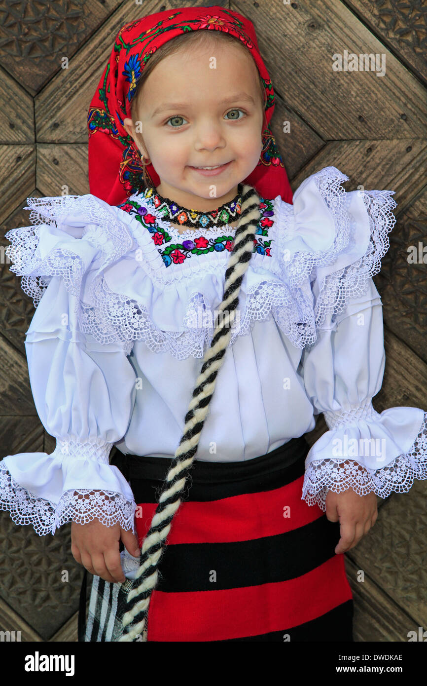 Petite fille portant des vêtements traditionnels roumains et fond de porte en bois traditionnel Banque D'Images