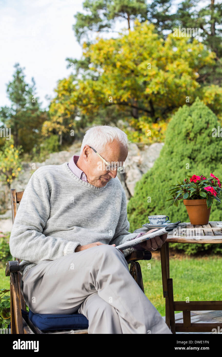 Senior man reading newspaper in yard Banque D'Images