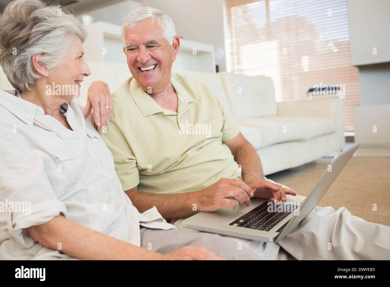 Cheerful senior couple en utilisant l'ordinateur portable ensemble assis sur un tapis Banque D'Images