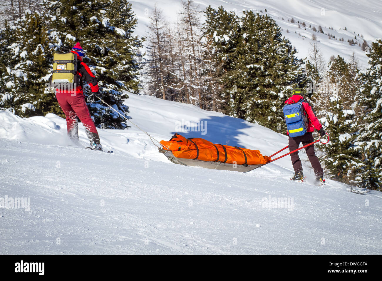 Deux membres d'une patrouille de ski aider un skieur blessé vers le bas de la montagne. Banque D'Images