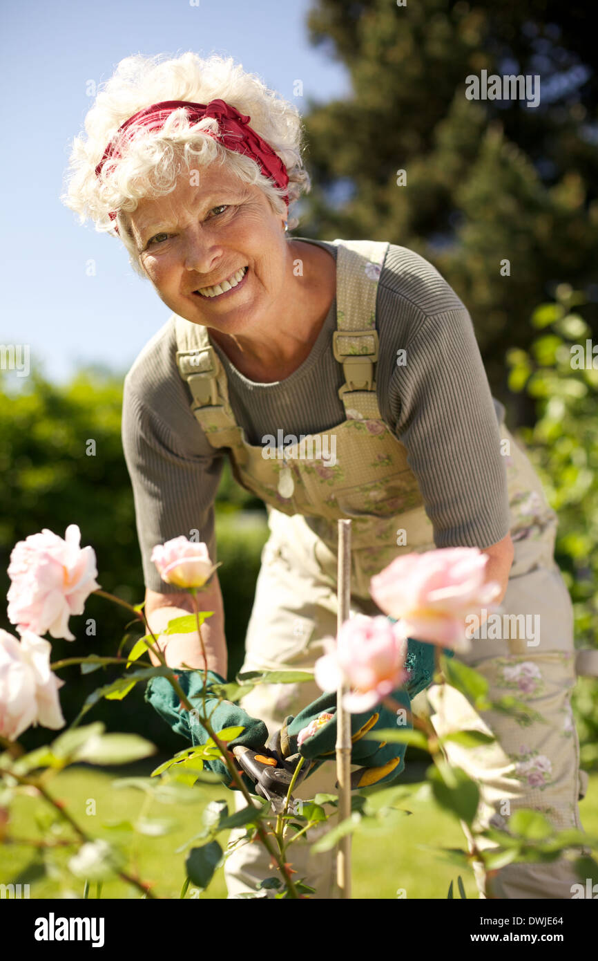 Portrait de jolie femme senior en prenant soin des plantes dans son jardin vous regarde en souriant - woman in backyard Banque D'Images