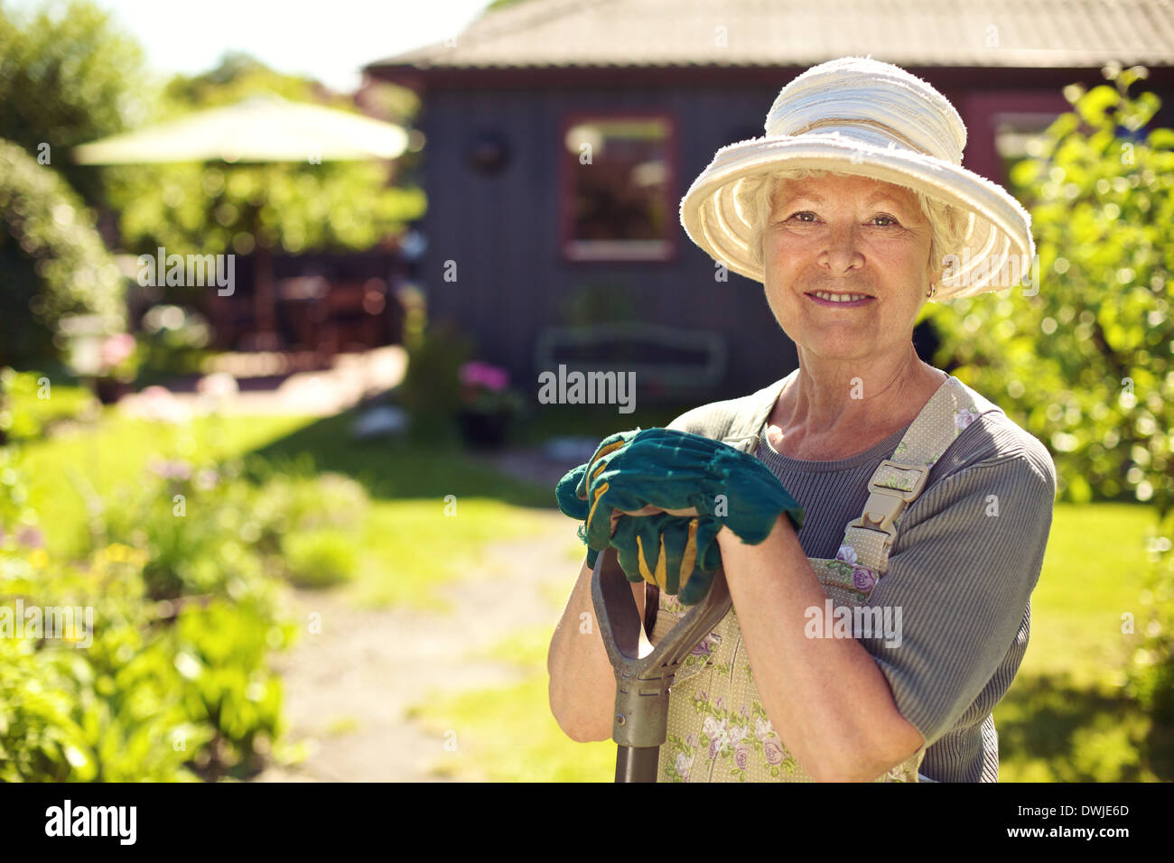 Portrait of senior woman wearing hat avec les outils de jardinage à l'extérieur. La femme debout avec une pelle dans son jardin jardin Banque D'Images