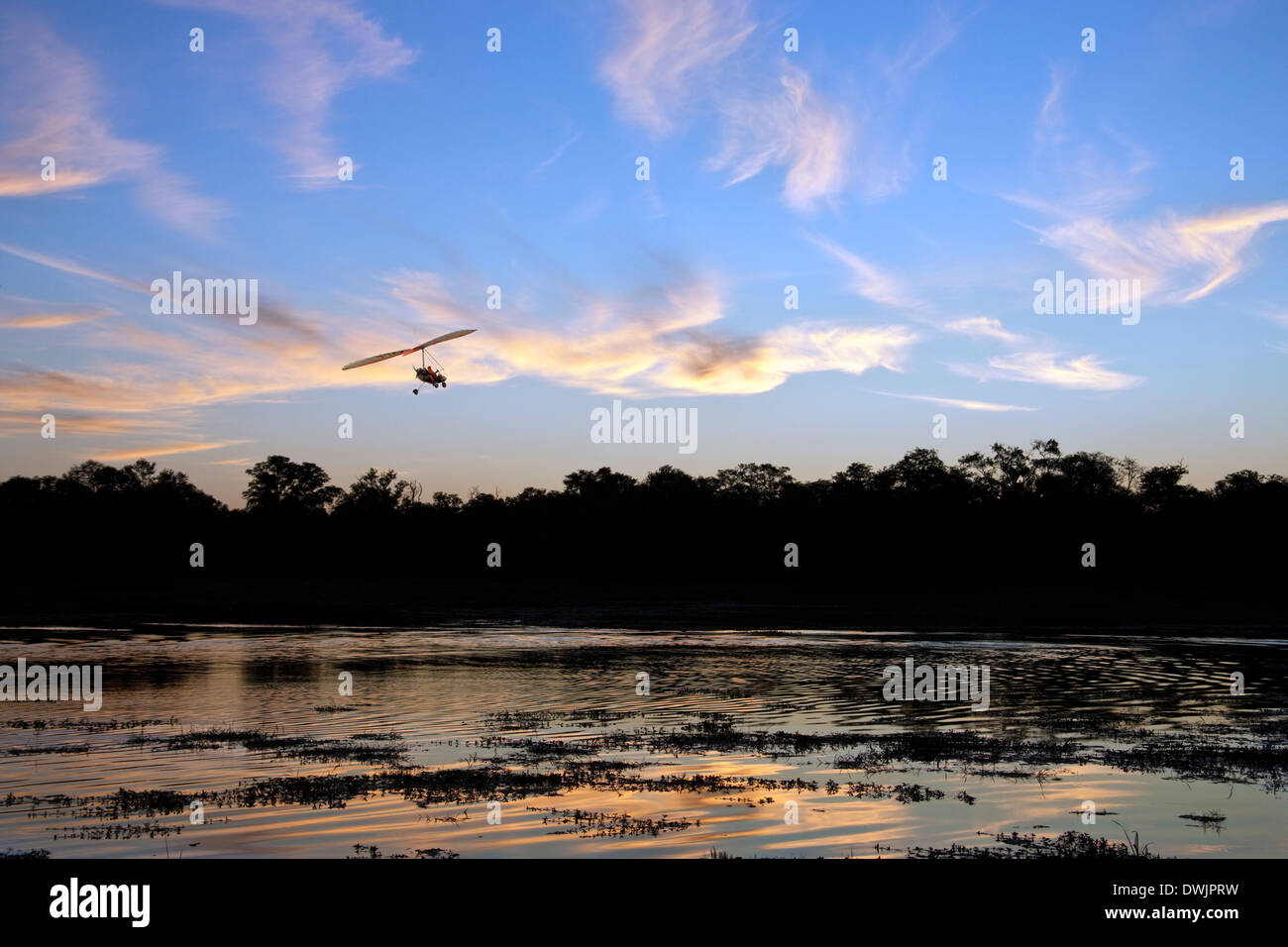 Un ULM avion volant au-dessus d'un canal dans le Delta de l'Okavango au Botswana au coucher du soleil Banque D'Images