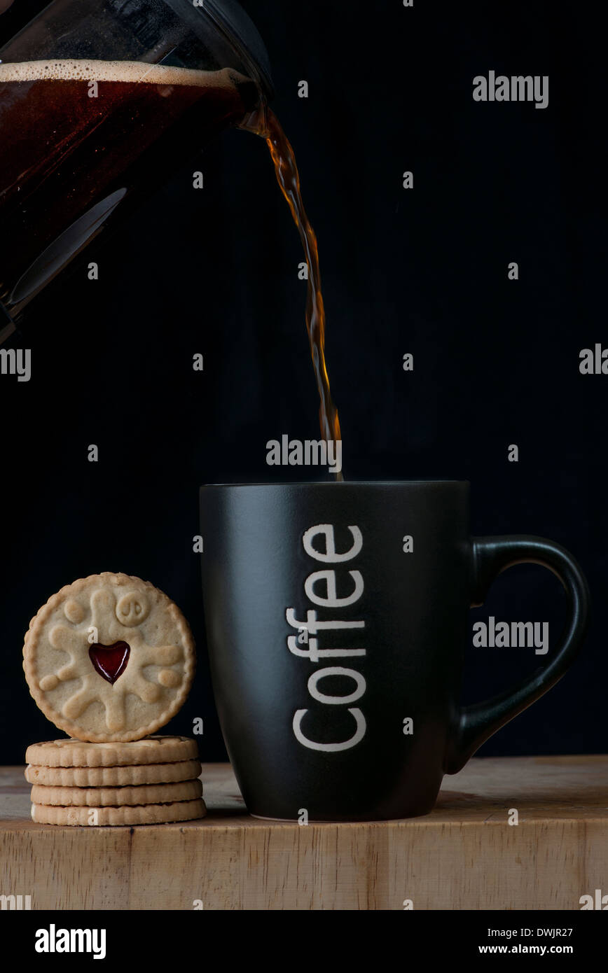 Verser du café d'une cafetière dans un mug et biscuits Banque D'Images