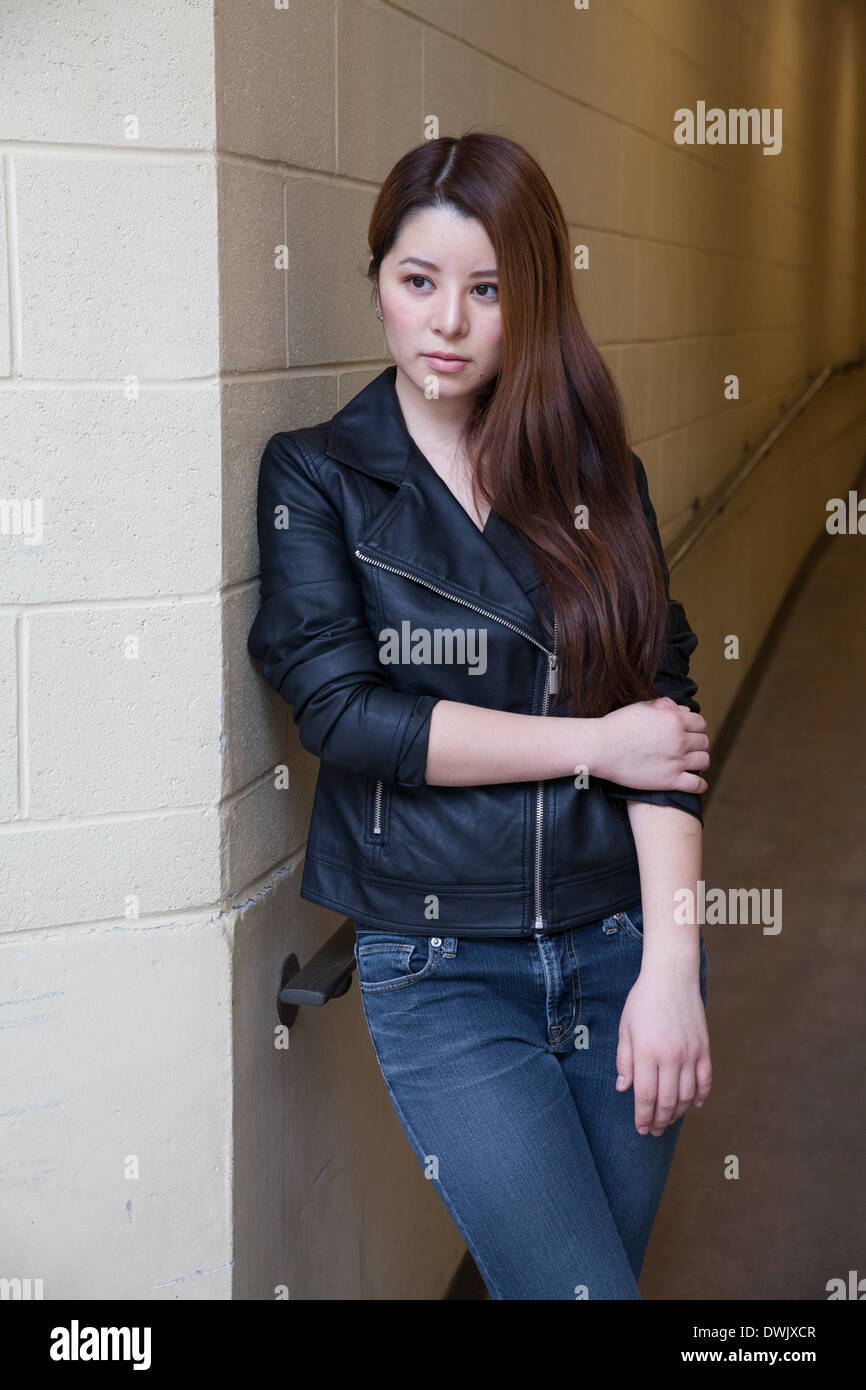 Asian Woman in Black veste en cuir et jean bleu appuyé contre le mur Banque D'Images