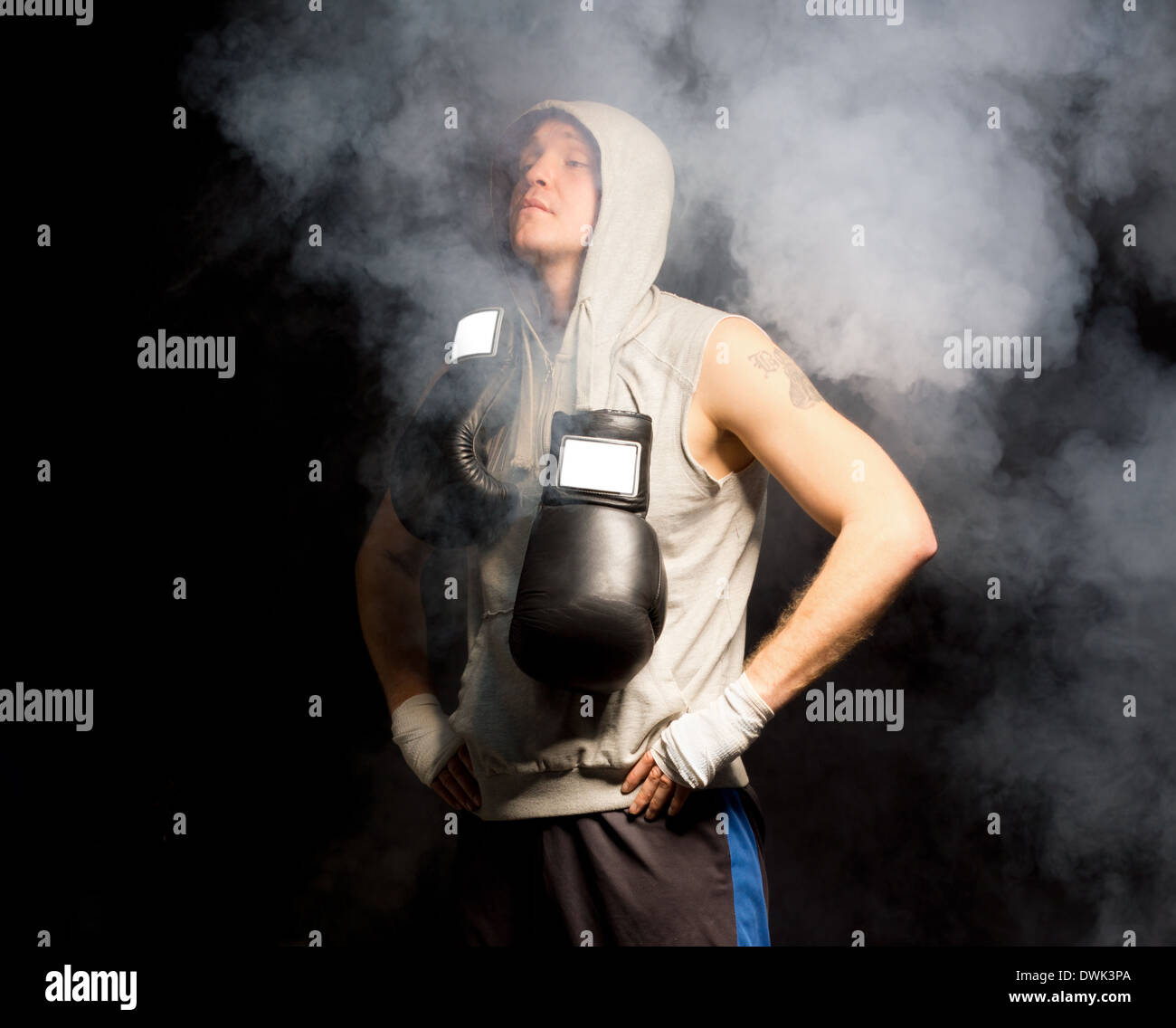 Jeune boxeur debout dans une atmosphère enfumée, respirant profondément pour calmer ses nerfs avant un combat avec ses gants se balançant autour de son cou. Banque D'Images