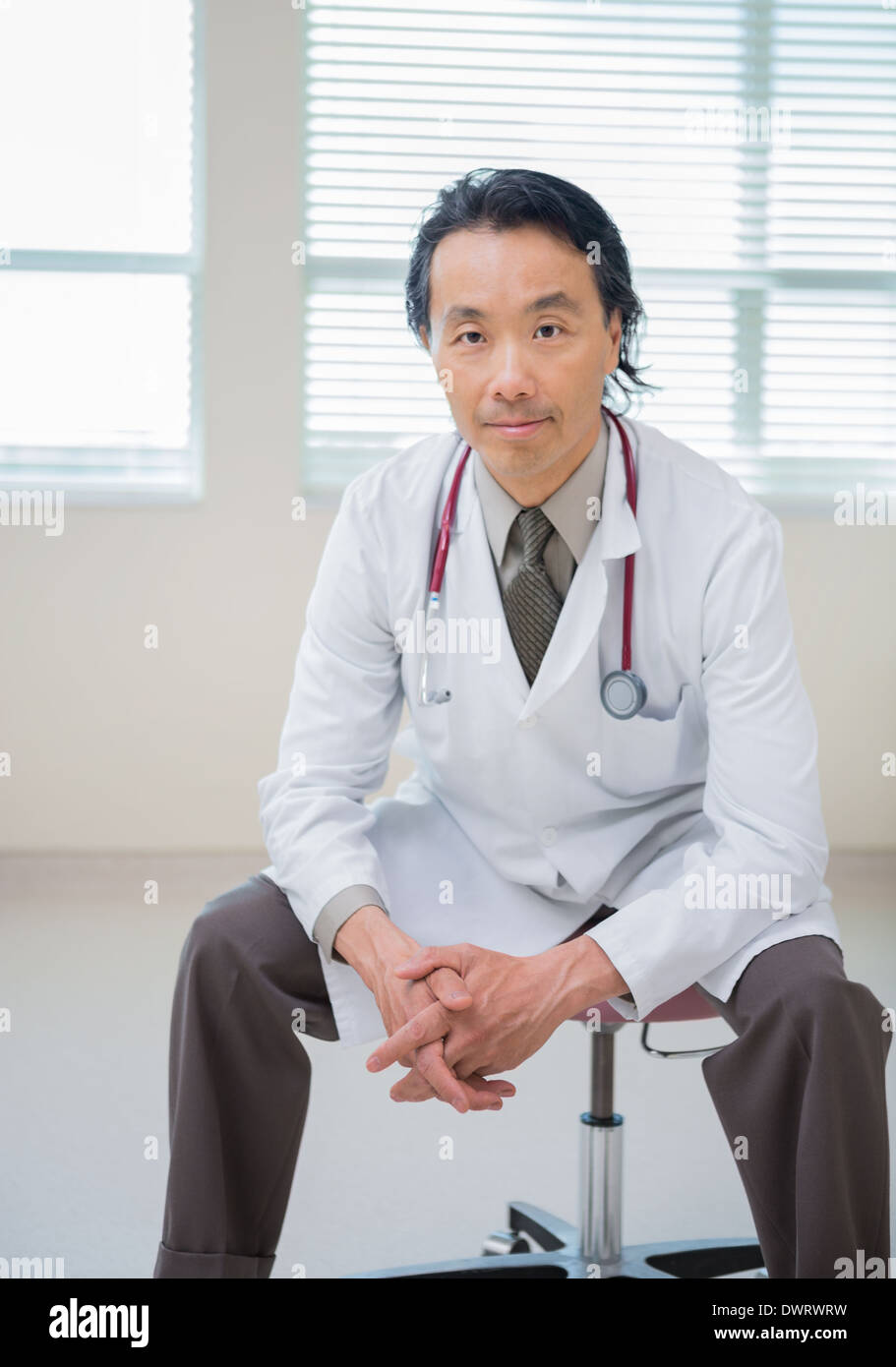 Doctor with hands clasped sitting in hospital room Banque D'Images