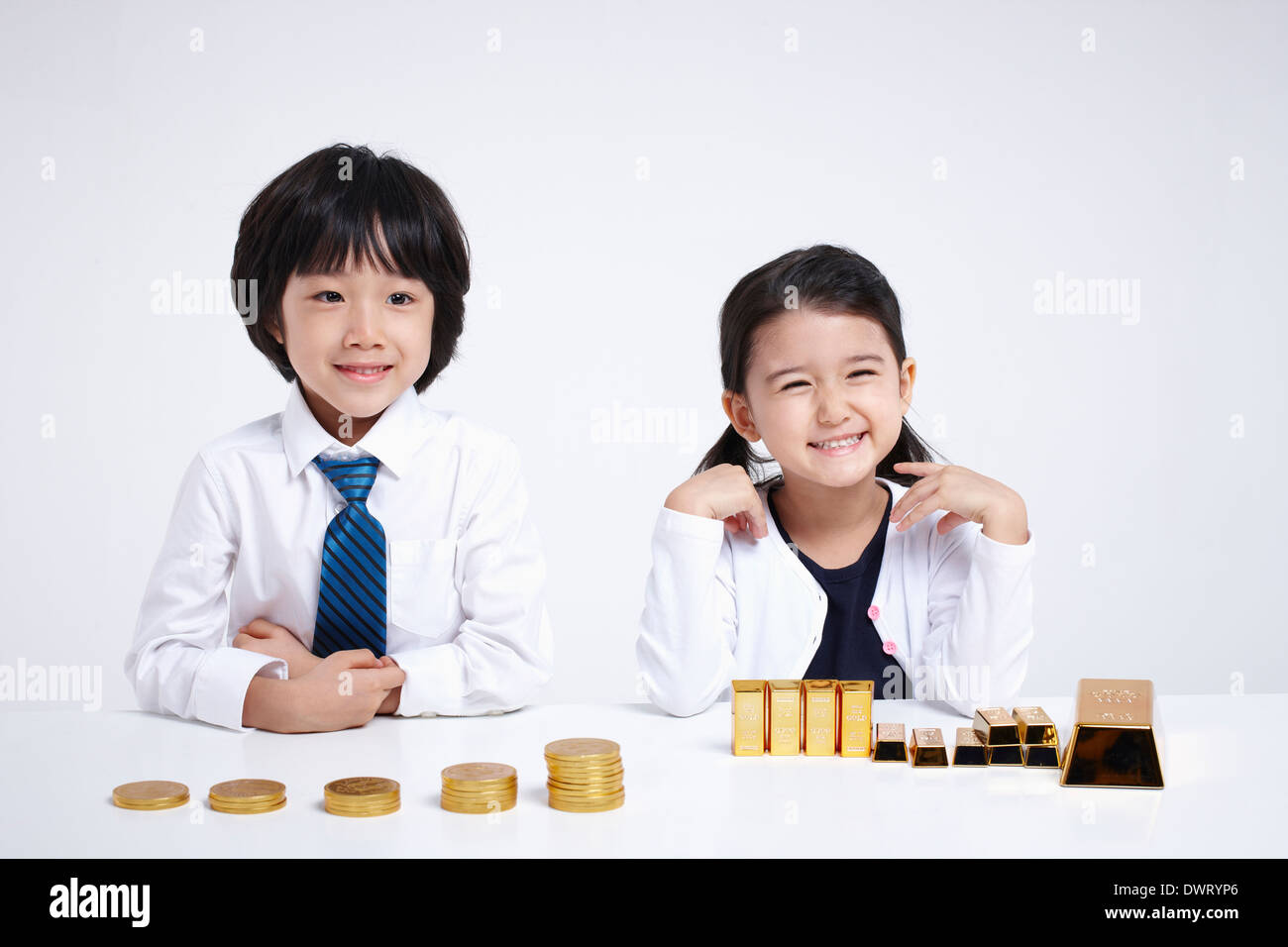 Les enfants portant des vêtements d'affaires à une table avec des pièces de monnaie et des lingots d'or Banque D'Images