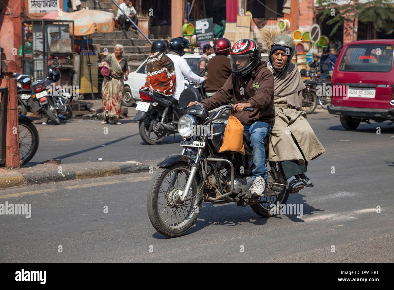 Jaipur, Rajasthan, Inde. Le trafic de la rue de la mi-journée dans le centre de Jaipur. Vieil Homme obtenir un trajet sur une moto. Banque D'Images