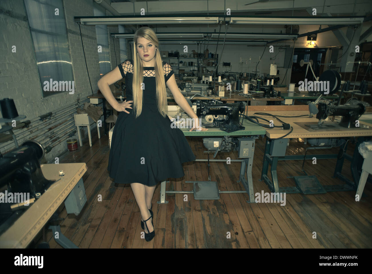 Un 16-year-old woman wearing a black vintage robe, s'oppose à une vieille machine à coudre dans l'usine corset Cortland. Banque D'Images