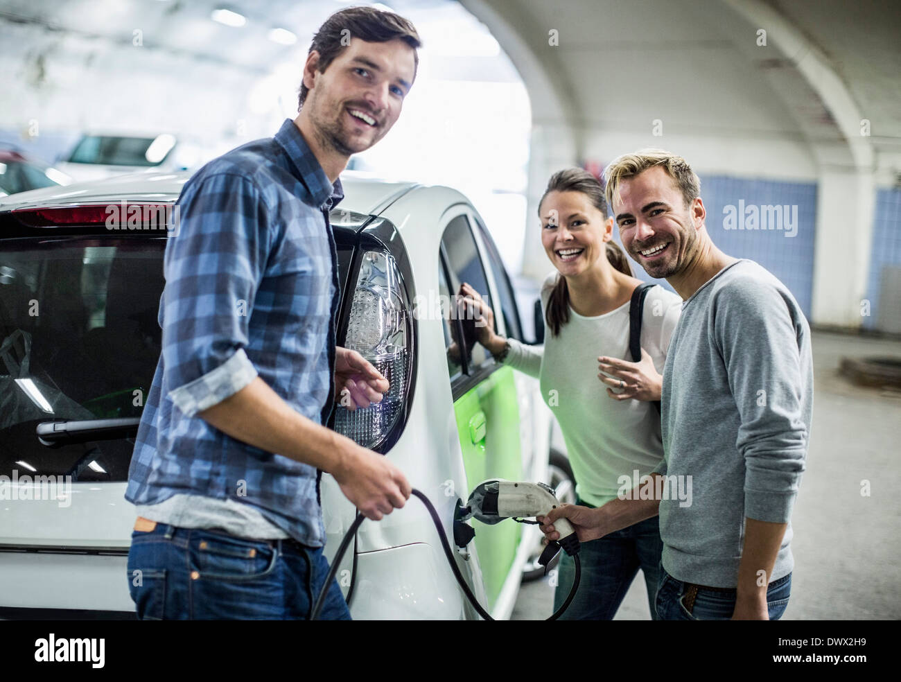 Portrait of happy friends avec l'homme à la voiture électrique de charge station de gaz Banque D'Images