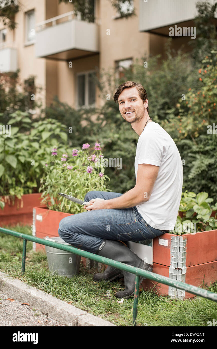 Portrait de jeune homme assis dans l'équipement de jardinage avec jardin Banque D'Images