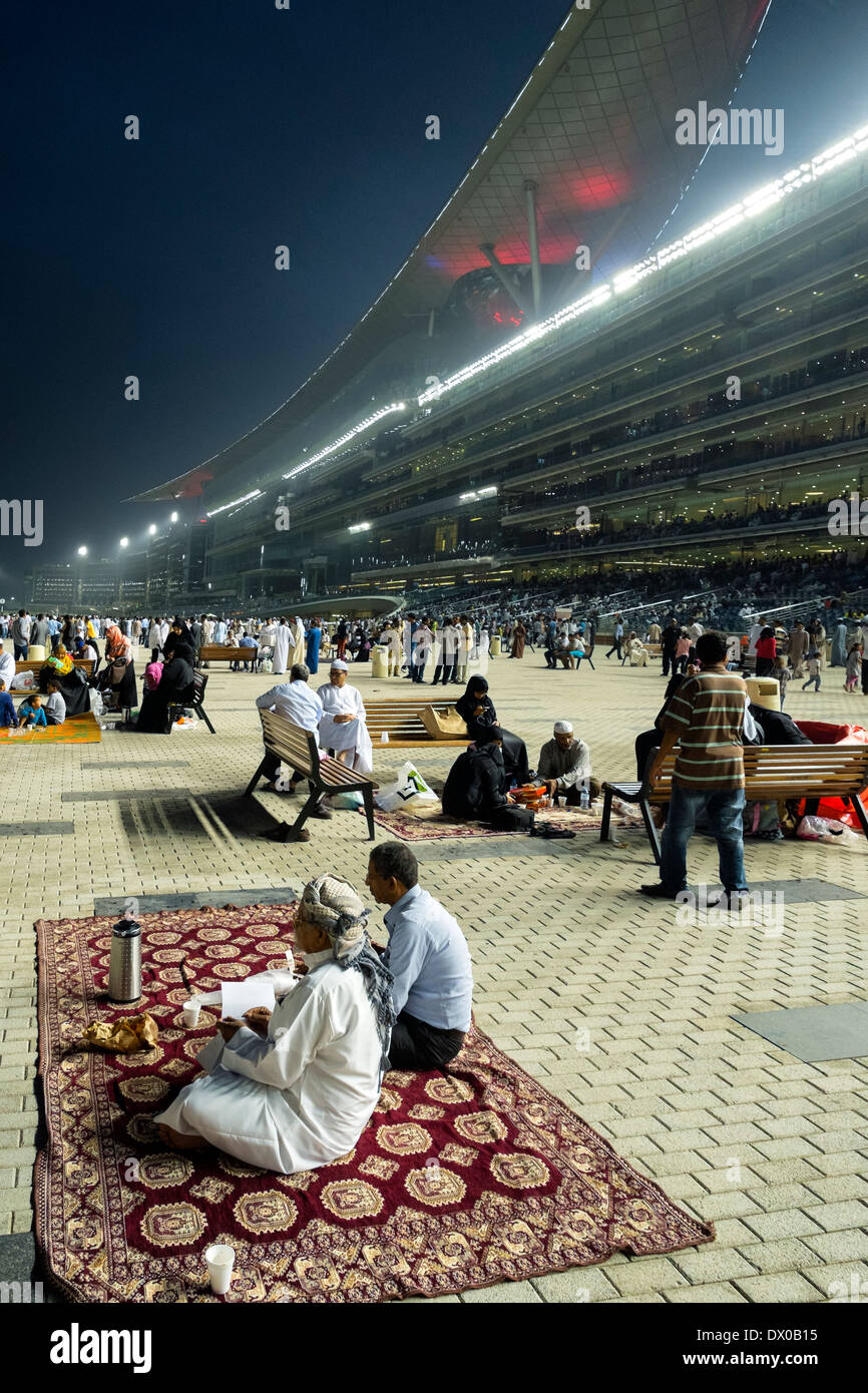 Les spectateurs et les courses de chevaux à la tribune réunion à l'hippodrome de Meydan Al nuit à Dubaï Émirats Arabes Unis Banque D'Images