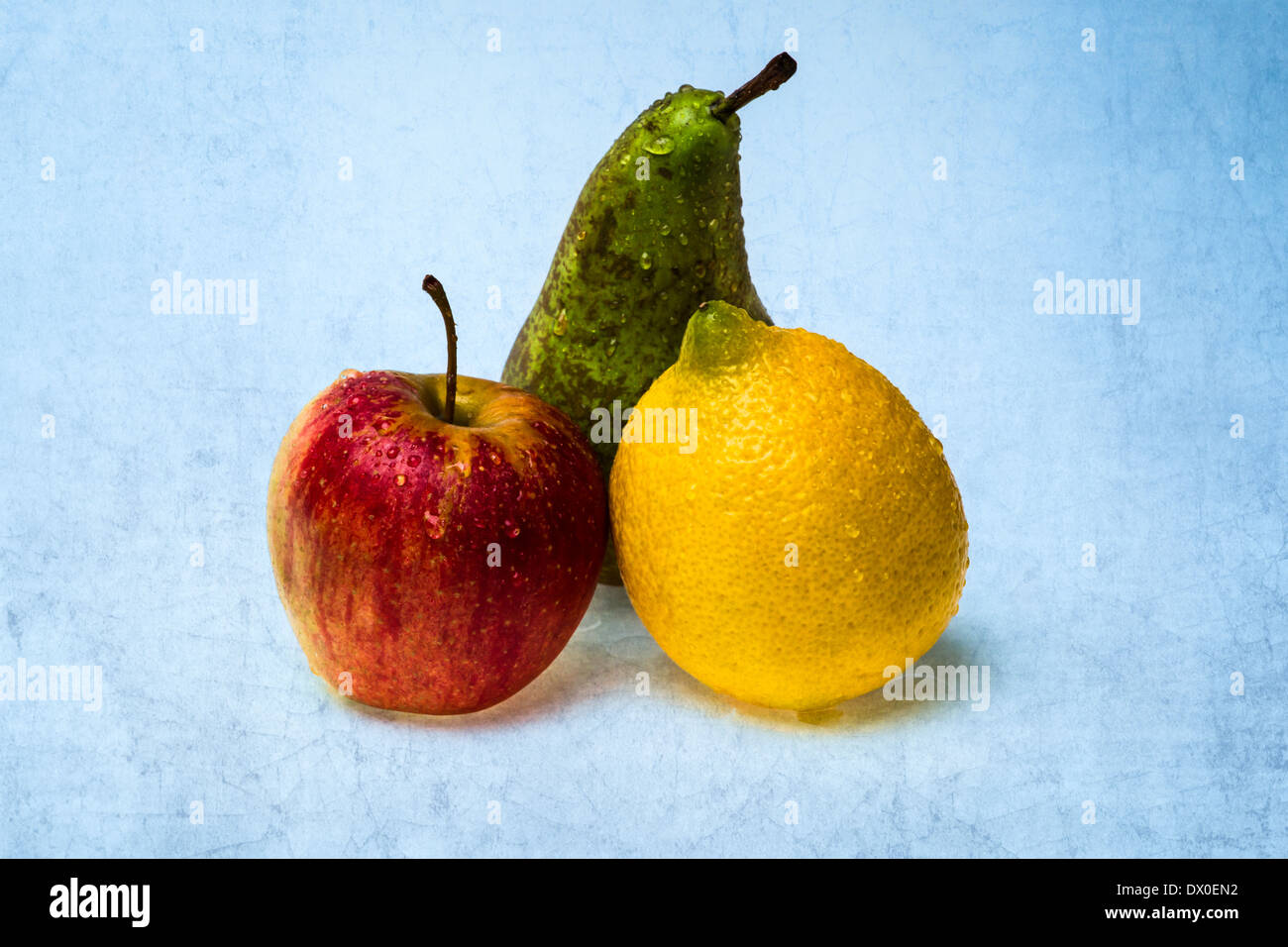 Citron, pomme, poire. Groupe de trois fruits ou rouge, jaune et vert couleurs texturées contre fond bleu. Banque D'Images