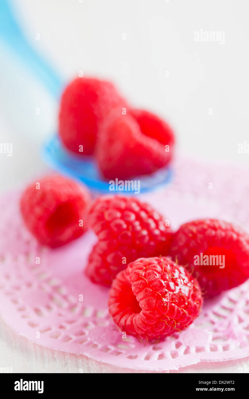 Gros plan du tas de framboises rouges frais avec cuillère en plastique bleu reposant sur le tapis rose décorative sur la surface d'éclairage Banque D'Images