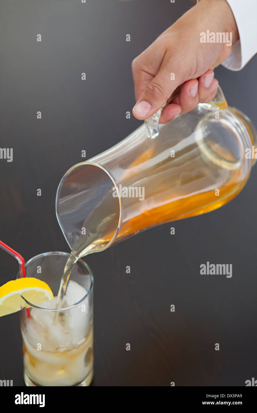 La main de l'homme de verser du thé glacé de cruche dans verre avec citron sur fond noir, high angle view, Close up Banque D'Images