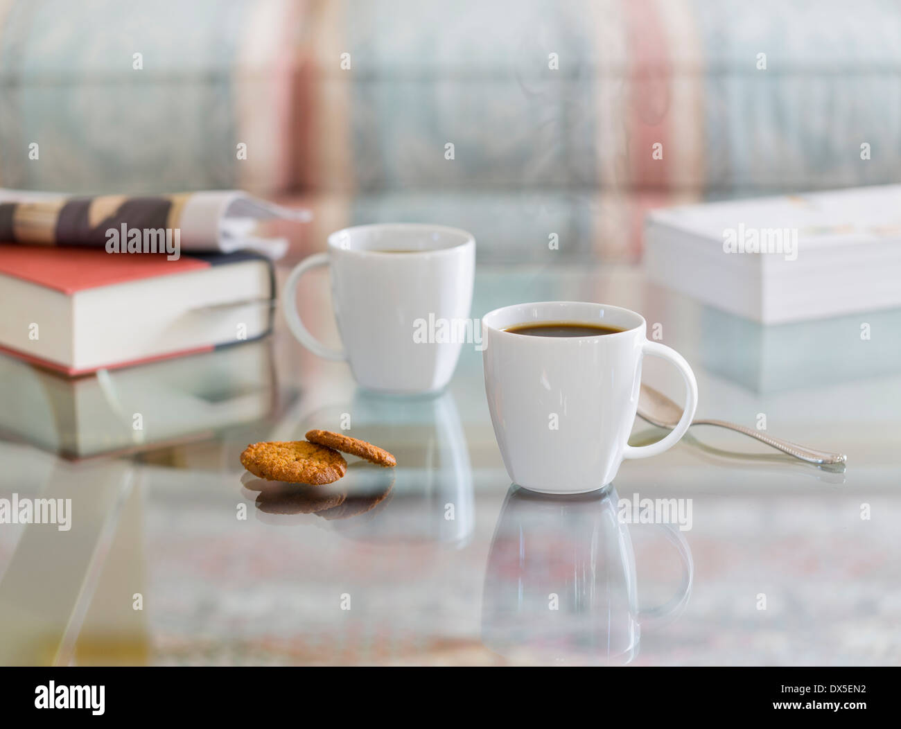 Les tasses de café sur une table en verre avec des biscuits au gingembre et à la cuillère. Livres et journaux dans l'arrière-plan Banque D'Images