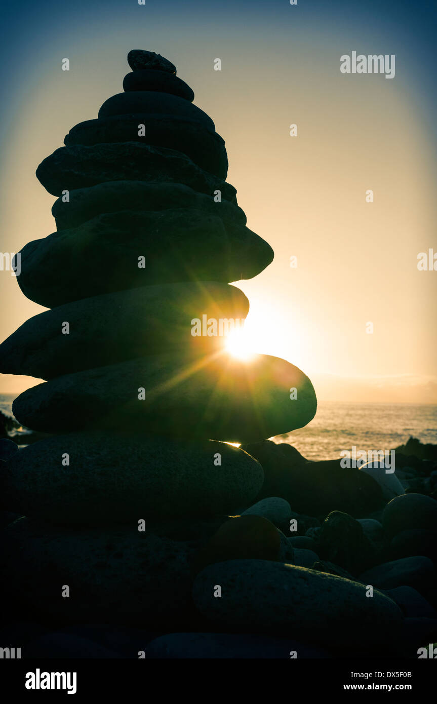 Des pierres en équilibre sur plage et du soleil au coucher du soleil. Banque D'Images