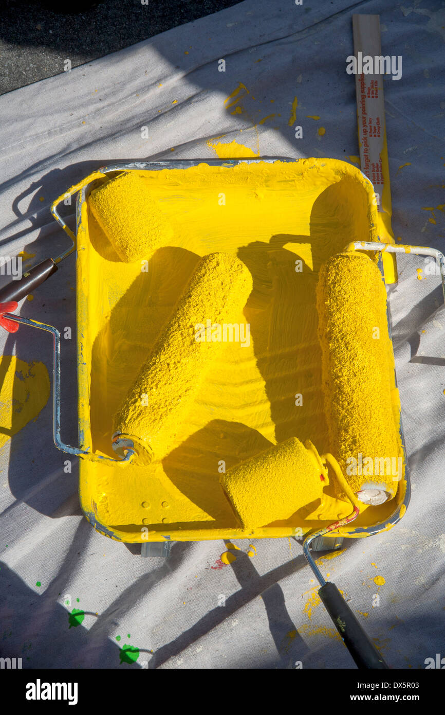 Un rayon de soleil qui brille sur rouleaux de peinture dans une casserole de peinture jaune sur une bâche dans un lieu de travail. Banque D'Images