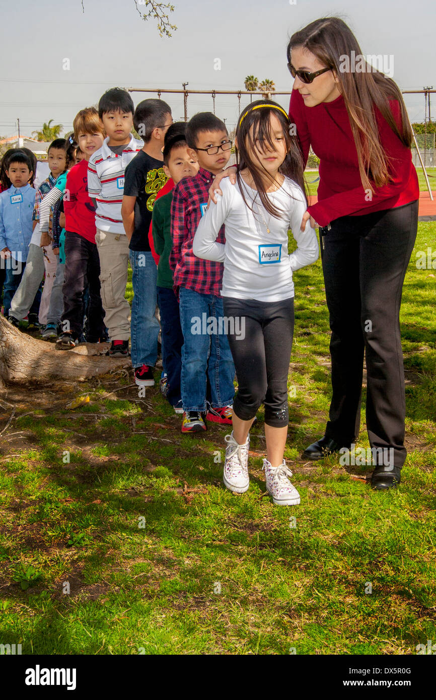 Un enseignant et sa cuisine asiatique et hispanique, de race blanche, les étudiants de première année jusqu'à une ligne patiemment Garden Grove, CA, aire de l'école élémentaire. Banque D'Images