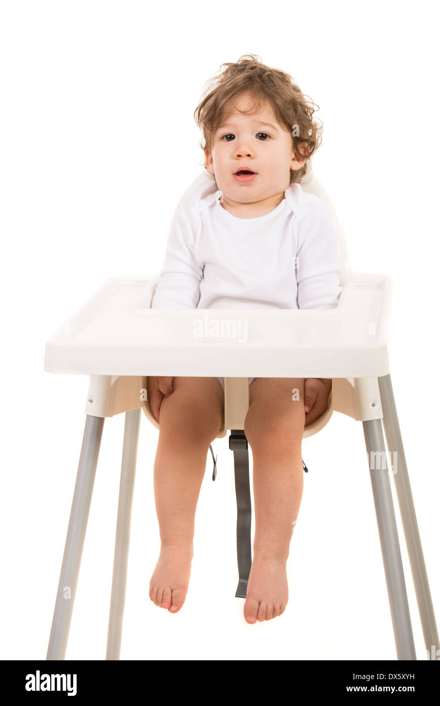 Surpris tout-petit garçon debout tout droit dans une chaise haute isolé sur fond blanc Banque D'Images