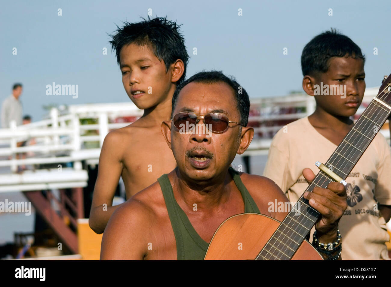 Un homme asiatique portant des lunettes de soleil est un jeu de guitare en bois sur les rives du Mékong à Phnom Penh, Cambodge. Banque D'Images