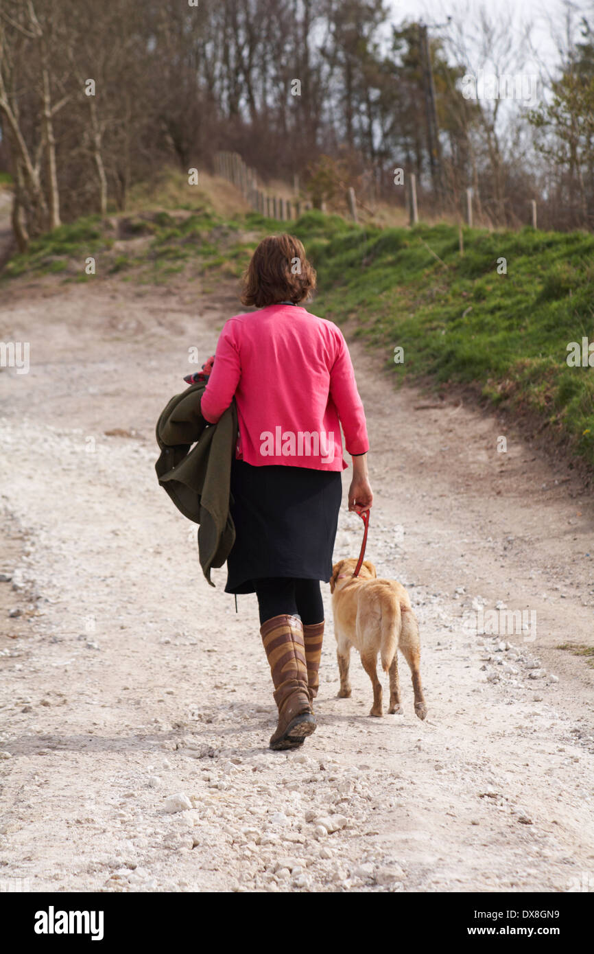 Femme de prendre le chien pour une promenade le long de chemin de campagne à Dorset en Mars Banque D'Images