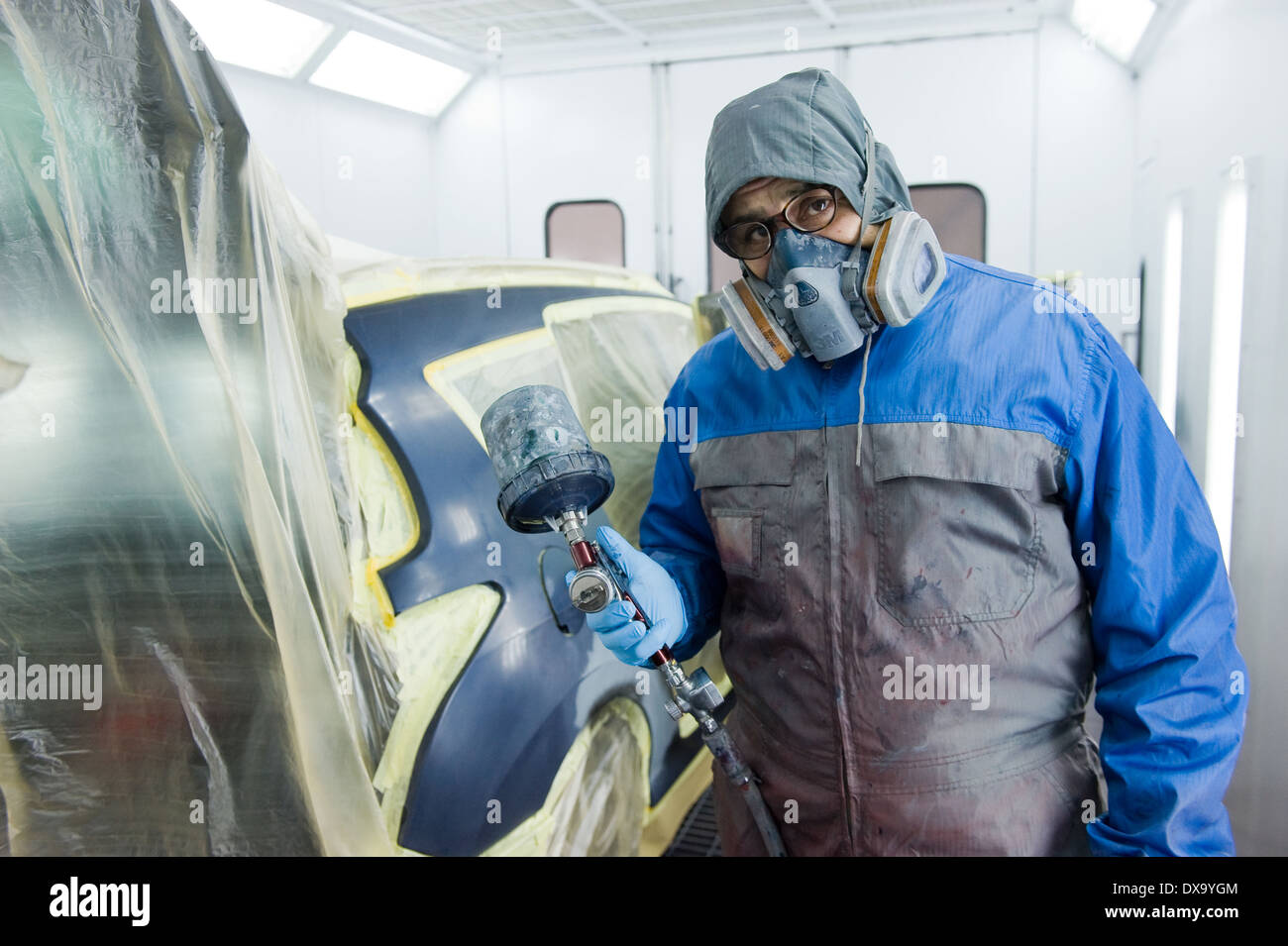 Une voiture qui est peintre professionnel peinture le travail du corps d'une voiture dans une boîte de peinture d'un garage avec un aérographe. Banque D'Images