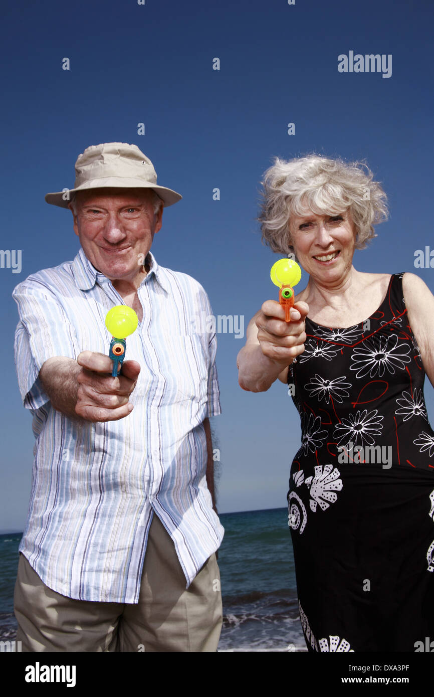 Senior couple on beach avec les pistolets à eau Banque D'Images