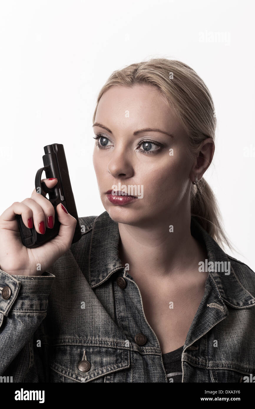 Blond woman holding handgun et à la recherche autour, portant veste en jean. Banque D'Images