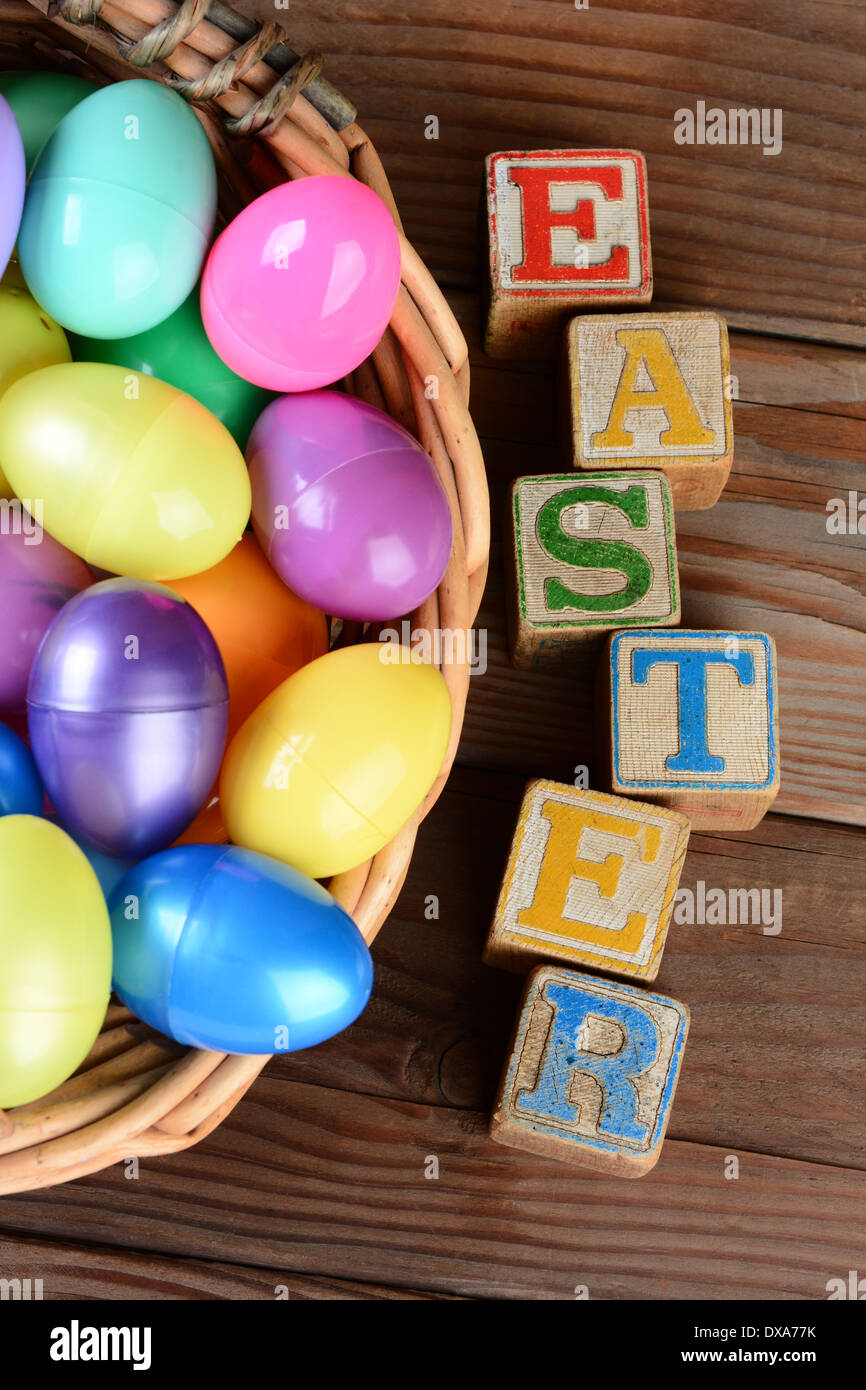 Le mot Easter énoncés dans les blocs de jouets pour enfants et un panier plein d'œufs en plastique. Format vertical sur une table en bois rustique. Banque D'Images