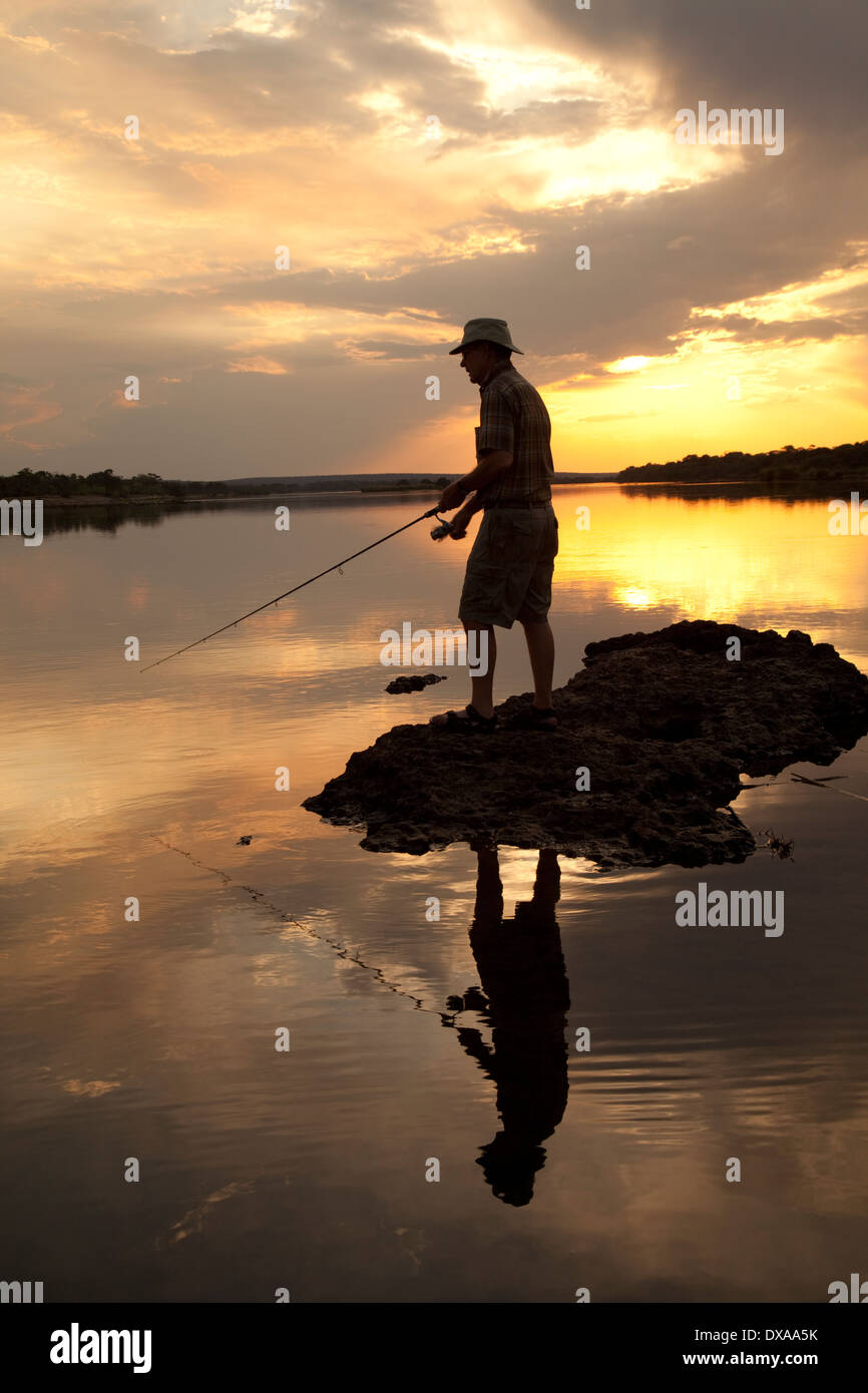 Silhouette de pêcheur La pêche dans la rivière Zambèze au coucher du soleil près de Livingstone en Zambie Banque D'Images
