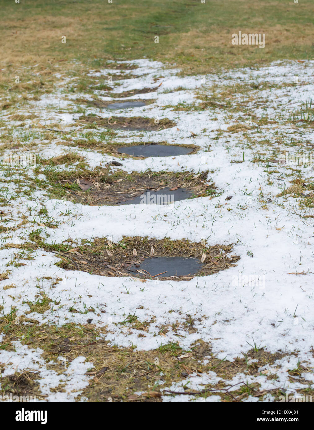 Chemin givré avec de la neige fondue et l'ardoise des tremplins menant à l'herbe verte. Banque D'Images