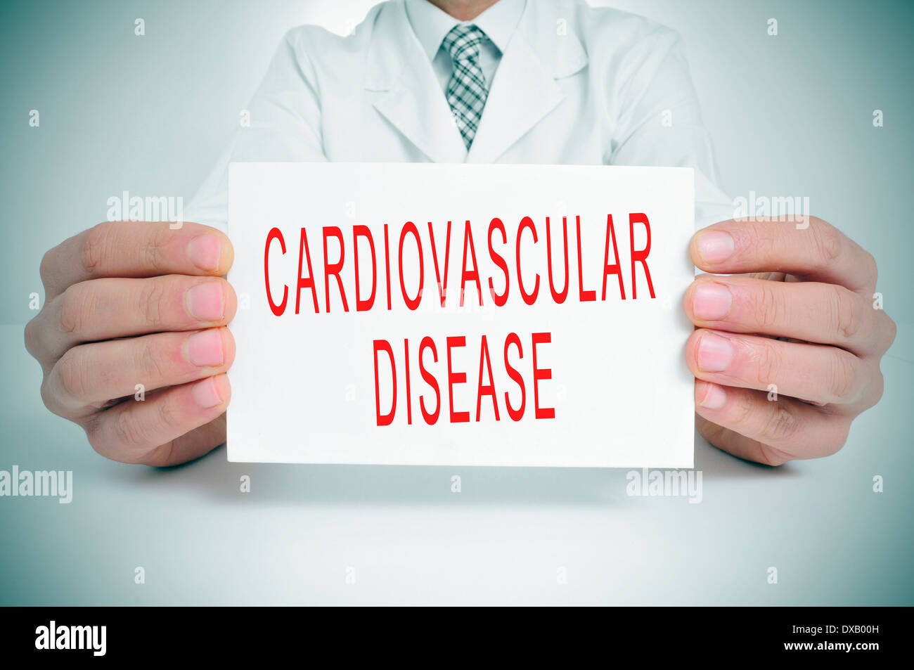 Un homme portant un manteau blanc assis dans un bureau avec une pancarte portant le texte les maladies cardiovasculaires écrit en c Banque D'Images